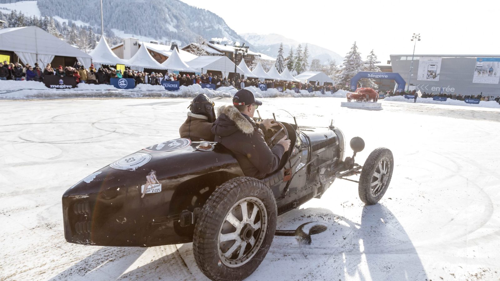 Un homme au volant d'une voiture vintage sur une route couverte de neige, créant une scène hivernale charmante.