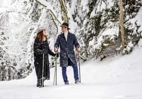 couple élégant avec un chapeau en promenade dans un paysage enneigé sous les sapins