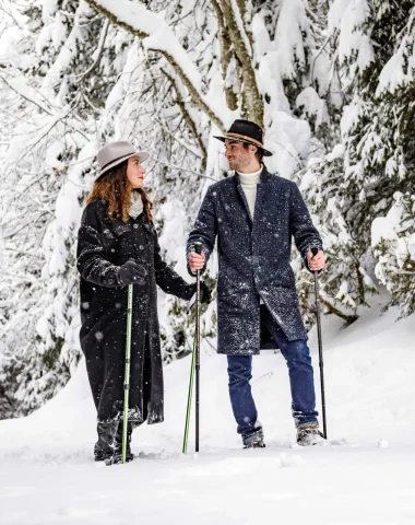 couple élégant avec un chapeau en promenade dans un paysage enneigé sous les sapins