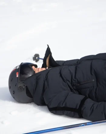 femme allongée se reposant dans la neige avec une tenue de ski noire