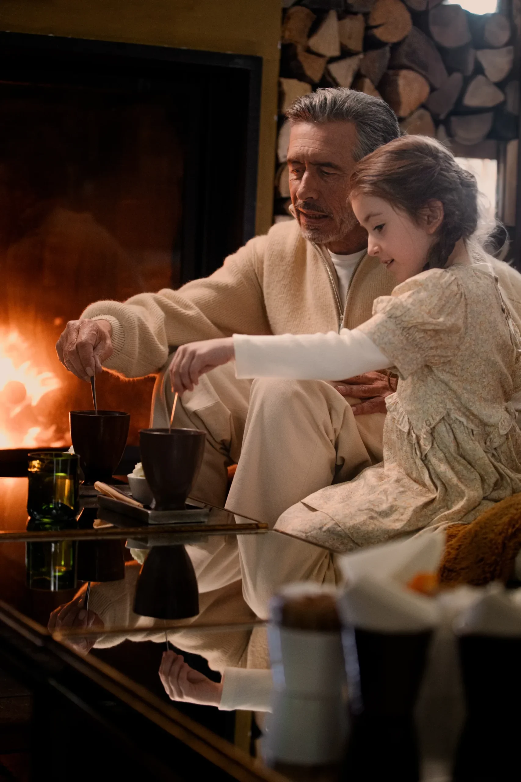 grand père et sa petite fille qui boivent un chocolat chaud devant un feu de cheminée